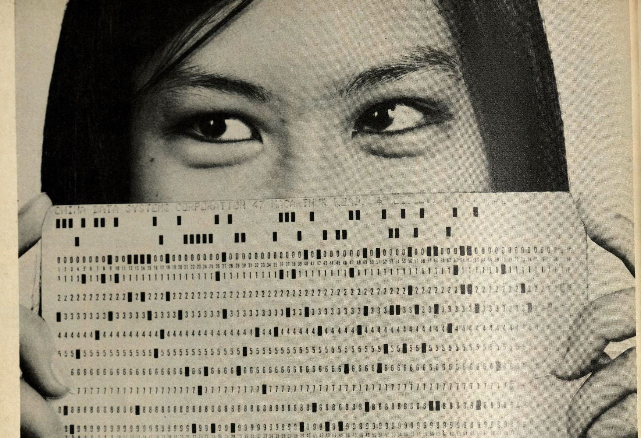 Scanned image of the magazine ad for China Data Systems, illustrated by a photo of a woman holding a computer punchcard in front of her mouth and nose, so that only her eyes and hairline are visible.